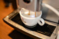 Een wit kopje staat op het lekrooster van een espressomachine, met twee dunne stromen koffie die erin lopen.